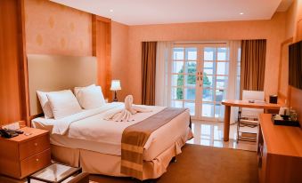 a large bed with a white and brown color scheme is in a room with a desk and sliding glass door at Portola Grand Renggali Hotel Takengon