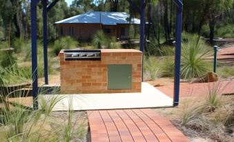 a brick walkway leads to a brick barbecue grill under a blue roof , surrounded by greenery and trees at Chalets on Stoneville