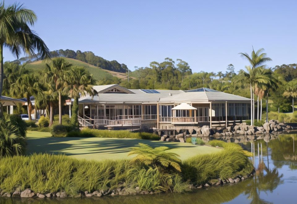 a large house with a green lawn and palm trees is surrounded by water , mountains , and palm trees at Pacific Bay Resort