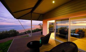 a wooden deck with two lounge chairs , a table , and a view of the ocean at sunset at Eco Beach Wilderness Retreat