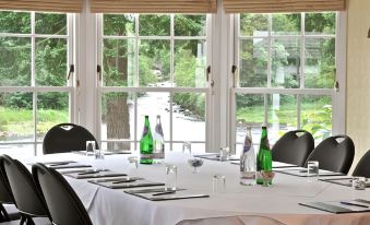 a long table with white tablecloth and green bottles is set up in a room with large windows at Banchory Lodge Hotel