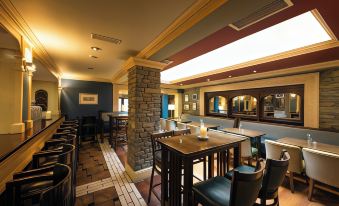 a well - lit restaurant with several tables and chairs , some of which are occupied by people at Castle Hotel Macroom