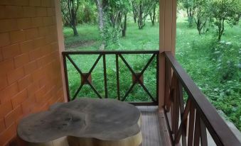 a wooden deck with a table and chairs , surrounded by green trees and grass , near a window that overlooks a forest at I Din Lake View Resort Nakhon Nayok