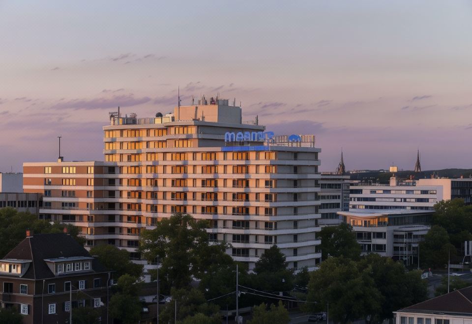 "a tall building with the word "" meetcan "" written on it is surrounded by trees and other buildings" at Maritim Hotel Darmstadt