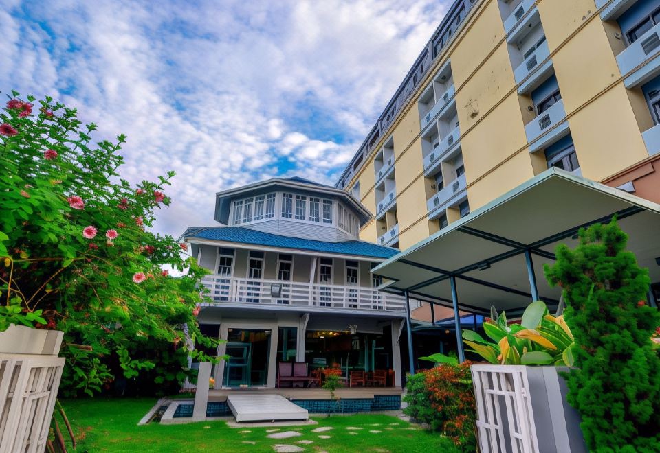 a modern , three - story building with a blue roof and white walls , surrounded by lush greenery and modern outdoor furniture at Viva Hotel Songkhla