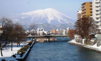 a snow - covered cityscape with a river running through it and a snow - capped mountain in the background at Hotel Metropolitan Morioka New Wing