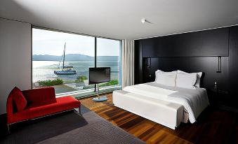 a modern bedroom with a large window overlooking the ocean , featuring a bed and a red couch at Altis Belem Hotel & Spa, a Member of Design Hotels