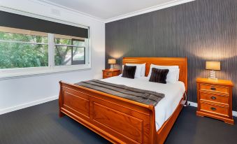 a large bed with a wooden headboard and footboard is situated in a bedroom with a window at Lake Wendouree Luxury Apartments