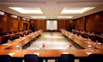 a large conference room with multiple rows of tables and chairs , a projector screen at the front , and empty desks at The Westlake Hotel & Resort Yogyakarta