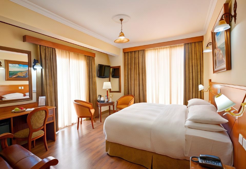 a spacious hotel room with a large bed , two chairs , a television , and a dining table at Semeli Hotel