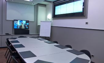 a conference room with a long table , chairs , and a tv mounted on the wall at Hotel Milano