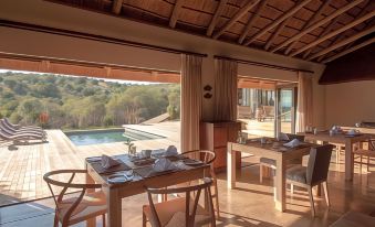 a dining room with a wooden table and chairs set up for a meal , overlooking a swimming pool at Bukela Game Lodge - Amakhala Game Reserve
