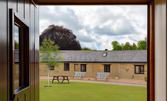 a view from an open window , looking out at a brick building with a grassy area and benches at Church Farm Lodge