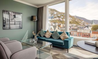 a modern living room with a blue couch , glass coffee table , and large windows overlooking a cityscape at Clarion Hotel Bergen
