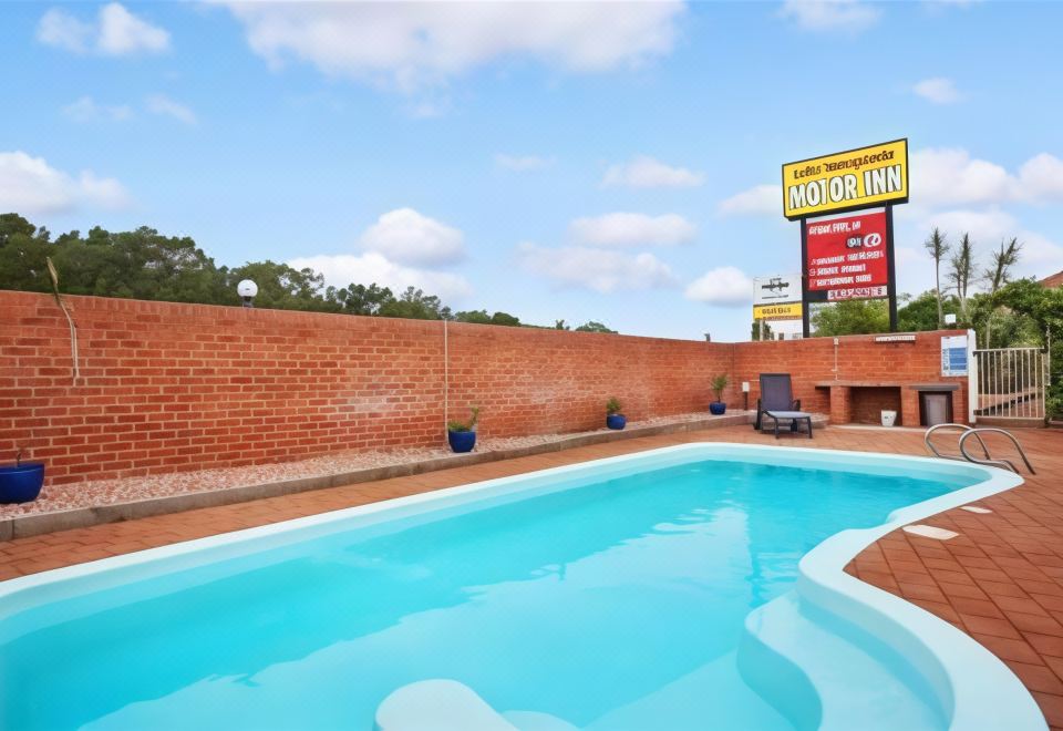 "a swimming pool with blue water , surrounded by a brick wall and blue sky , next to a sign advertising "" motorinn ""." at Lake Macquarie Motor Inn