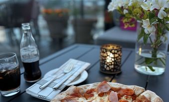a dining table with a pizza on it , accompanied by a glass of soda and a bottle of water at Quality Hotel Fredrikstad