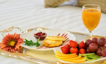 a tray with a glass of orange juice , plate of fruit , and a cup of tea is placed on a bed at Hotel Lulu