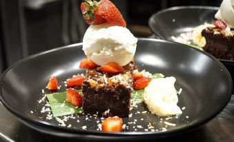 a black plate with a piece of chocolate cake topped with strawberries and whipped cream at Cairns Colonial Club Resort
