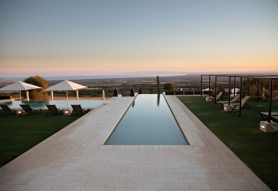 a large , empty swimming pool is surrounded by lounge chairs and a grassy area with a view of the sunset at Masseria Amastuola Wine Resort