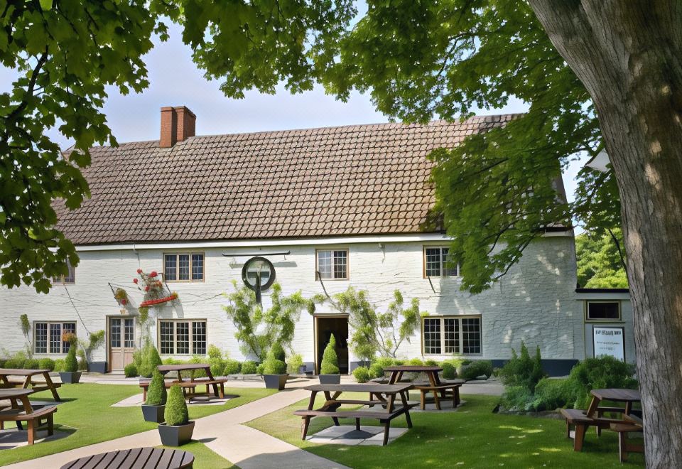 a white building with a red roof , surrounded by greenery and picnic tables , under a clear blue sky at The Orange Tree Thornham