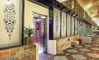 a hallway with a brick wall and a red carpet leads to an elevator with chinese - style decorations at Mercure Maitland Monte Pio