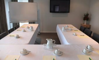 a conference room with multiple tables set up for a meeting , featuring white tablecloths , a pitcher , and several cups at Poenamo Hotel