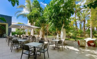 an outdoor dining area with several tables and chairs , surrounded by lush green trees and palm trees at Hotel Areca