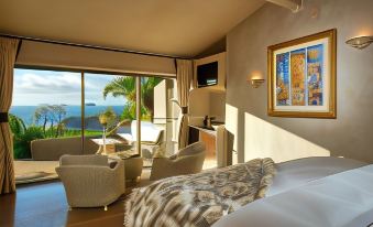 a luxurious bedroom with a king - sized bed , two chairs , and a large window overlooking the ocean at Delamore Lodge
