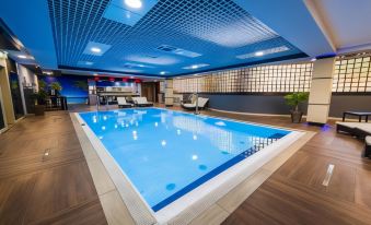 a large indoor swimming pool with a blue tiled ceiling and a wooden floor , surrounded by lounge chairs at Hotel Holiday