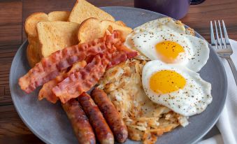 a plate of breakfast food , including eggs , bacon , sausage , toast , and toast , is presented on a wooden table at Hotel Valentino