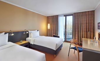 a modern hotel room with two beds , white bedding , and a balcony view , accompanied by wooden furniture at Lindner Hotel Leverkusen Bayarena