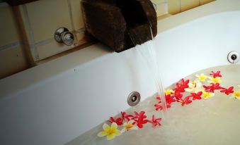 a wooden block with water flowing from it into a bathtub filled with flowers and foam at Parn Dhevi Riverside Resort & Spa