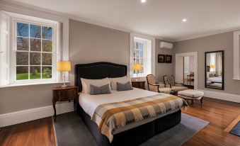 a large bed with a black headboard is in the middle of a room with two chairs and two windows at Quamby Estate