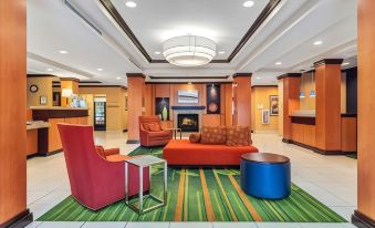 a hotel lobby with a check - in desk , a couch , and chairs arranged in an open space at Fairfield Inn & Suites Worcester Auburn