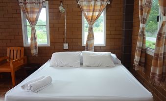 a large bed with white sheets and pillows is situated in a room with wooden walls and windows at I Din Lake View Resort Nakhon Nayok
