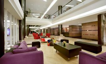 a modern hotel lobby with purple and red couches , chairs , and tables , as well as a reception desk at Aston Kupang Hotel & Convention Center