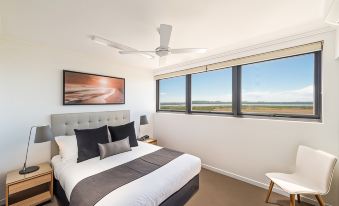 a modern bedroom with a large bed , white walls , and a view of the ocean through the large windows at Pacific Sands Apartments Mackay