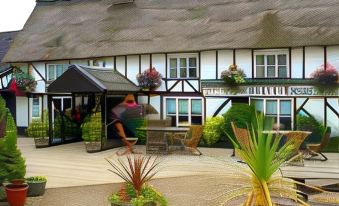a person walking past a thatched - roof building with plants and flowers on the front porch at The Willow House