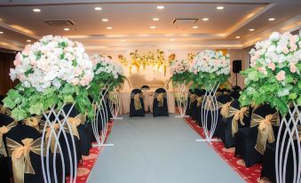 a well - decorated banquet hall with a large arch of flowers , black and white vases filled with white flowers , and a stage at Horison Express Sentani