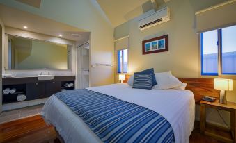 a large bed with a blue and white striped blanket is in a room with wooden floors at Exmouth Escape Resort