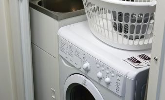 a white washing machine is situated next to a sink and a basket of laundry at Monterey Apartments Moranbah