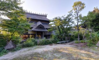 a large wooden house surrounded by trees , with a dirt path leading up to it at Shouen