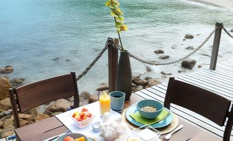 a dining table set up on a wooden deck overlooking the ocean , with a bowl of fruit and two glasses of orange juice at Aqua Nicaragua