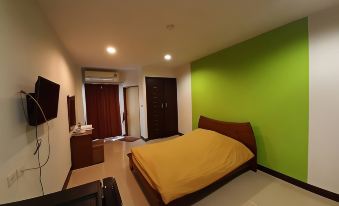 a modern bedroom with green walls , white tiled floor , and a large bed , as well as a desk area and tv at Thanarom Place