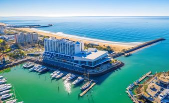 a large hotel situated on the beach , with boats docked in front of it and clear blue water surrounding it at Tivoli Marina Vilamoura