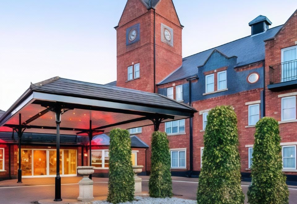 a large brick building with a clock tower , surrounded by trees and a covered entrance at The Park Royal Hotel & Spa