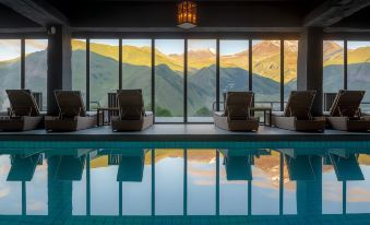 a large indoor pool surrounded by lounge chairs , with a view of the mountains outside at Rooms Hotel Kazbegi