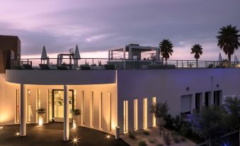 a modern building with a rooftop terrace , palm trees , and blue sky at dusk , illuminated by lights at Mercure Villeneuve Loubet Plage