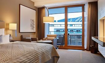 a hotel room with a king - sized bed , a chair , and a window overlooking the city at Kempinski Hotel Berchtesgaden