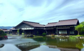 a large wooden building is situated next to a pond with water fountains in front at Ryugon